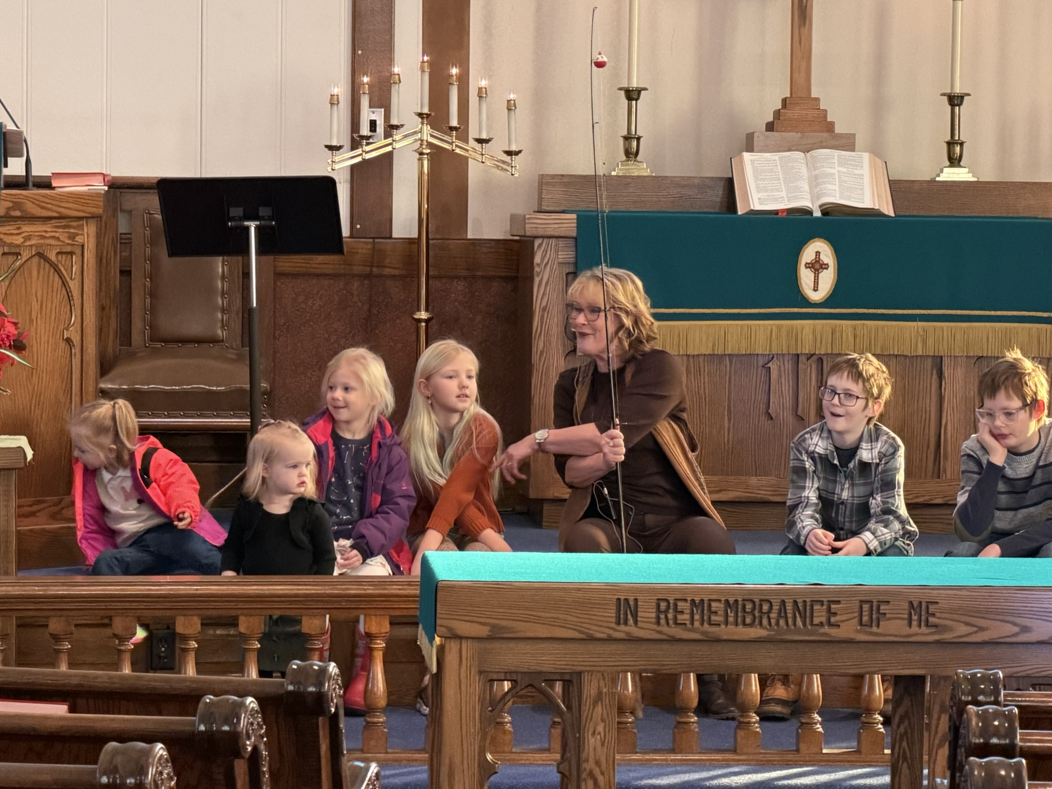 Children on stage with Pastor Paula as talks about being fishers of men during a children's church session