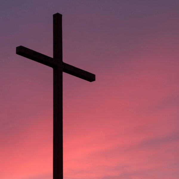 A silhouette of a cross stands against a pink and purple sunset sky.